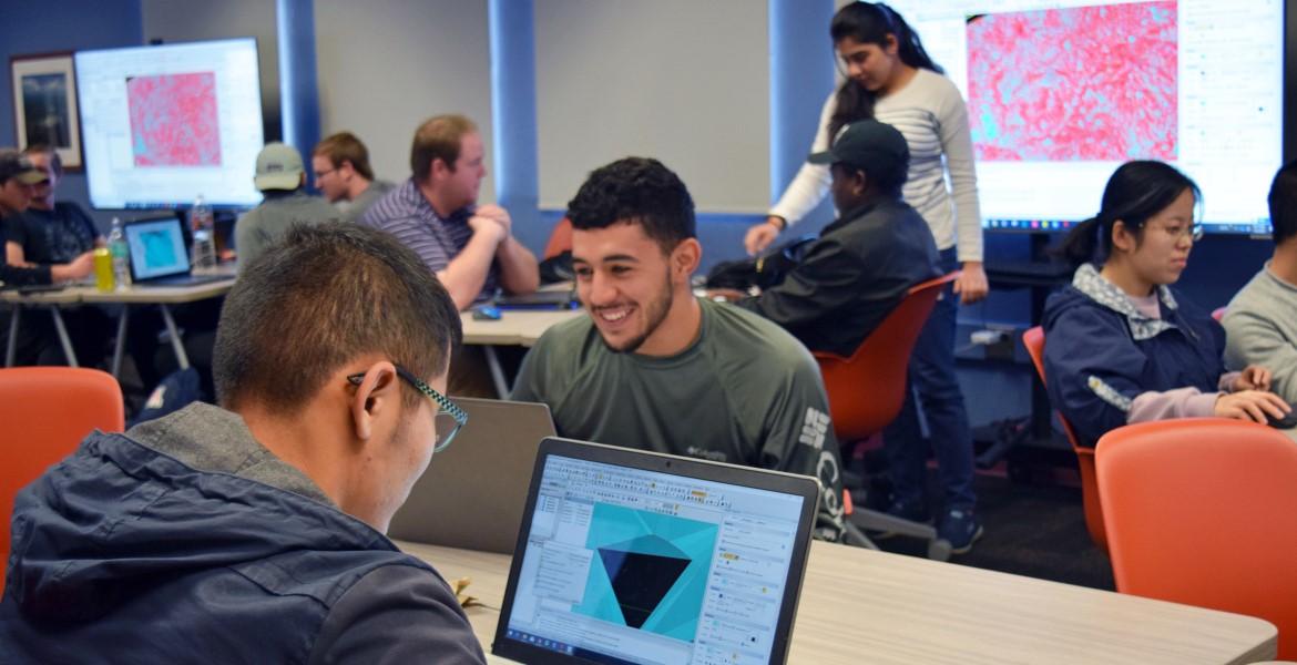 A students, seen from behind, looking at a rending of a mine plan on his laptop. He is in a classroom, and other students can be seen in the background.