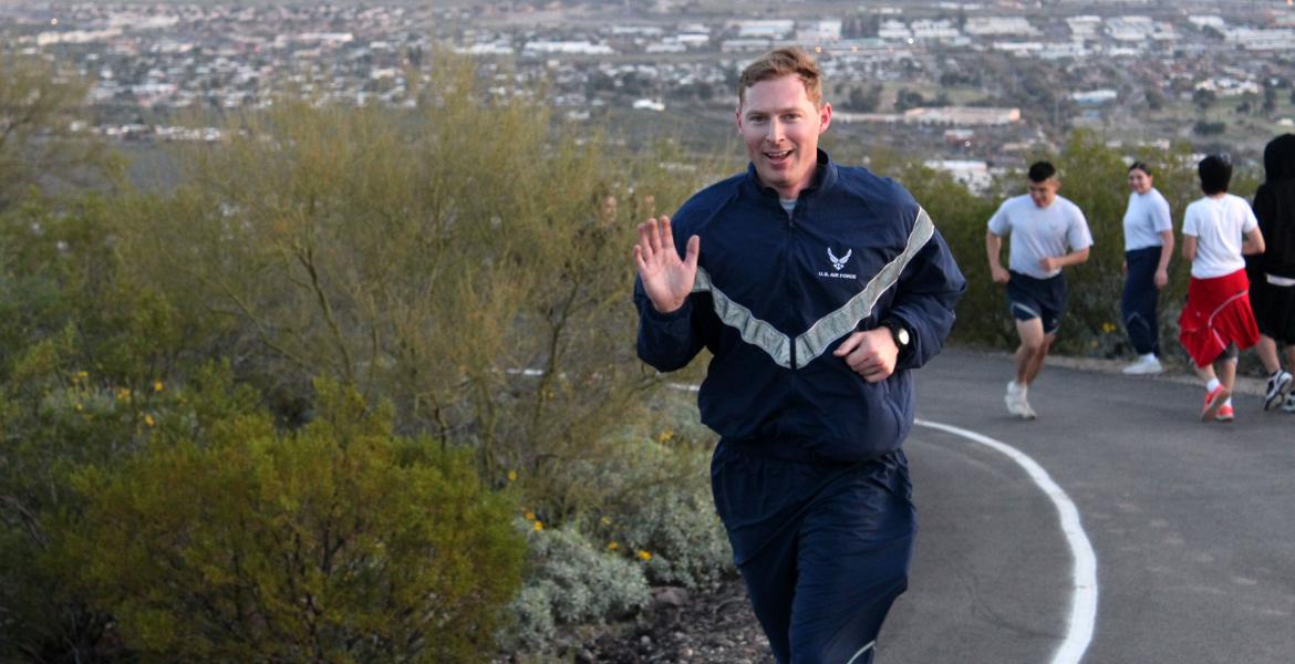 Ryan Raettig smiling and waving as he runs up Tumamoc Hill.