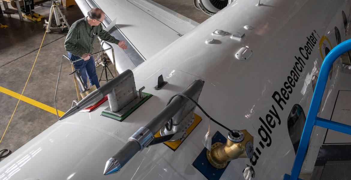 A photo shot from above of a man at the top of a ladder next to a large white airplane, which says 