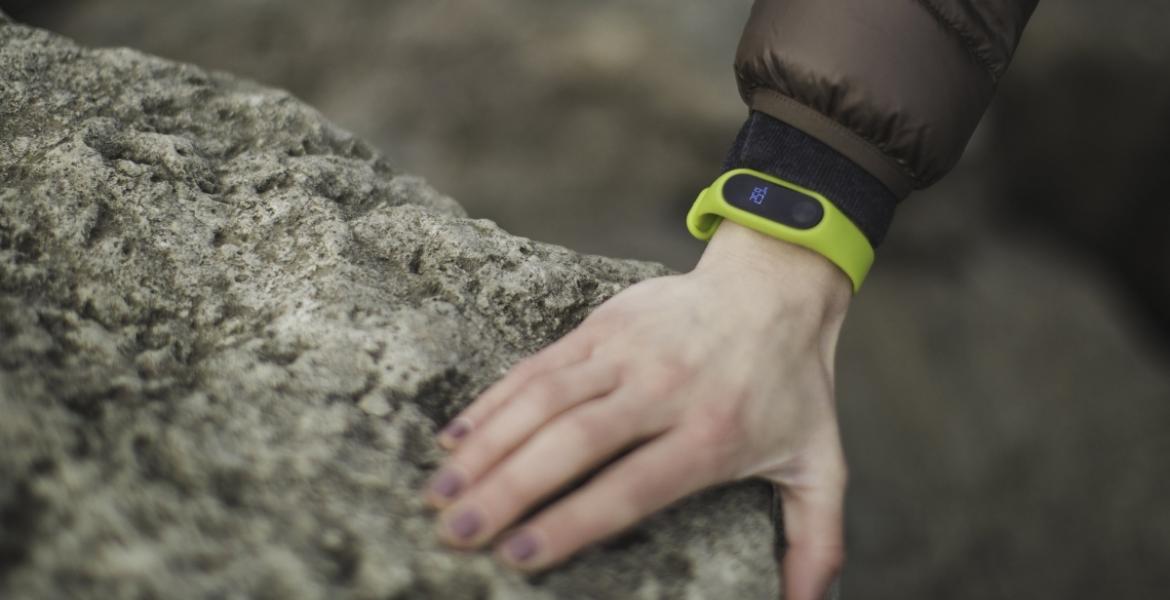 A close-up of a hand resting on a rock. There is a green smartwatch on the wrist.