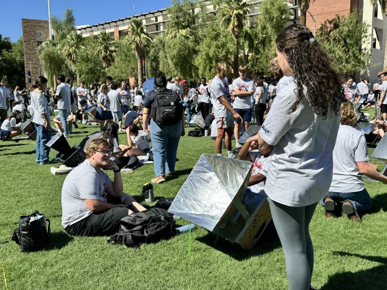 Students watch their handmade ovens convert solar energy into heat on a grassy lawn.