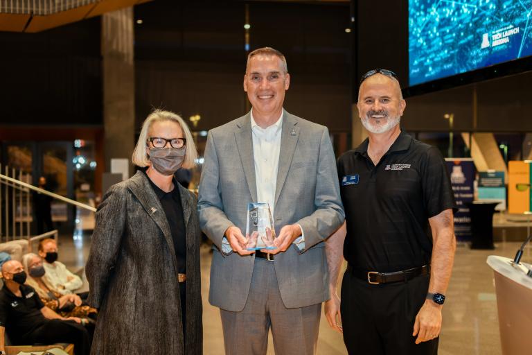 A woman and two men smile for a photo. Mark Van Dyke, center, is holding a glass award.