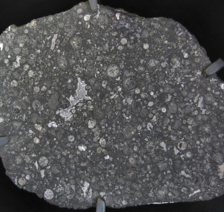 cross section of a meteorite -- looks similar to spotty or gravely black asphalt on a playground.