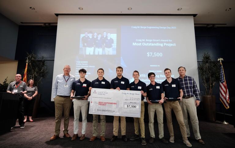 A group of students stands on a stage holding a giant, $7,500 check.