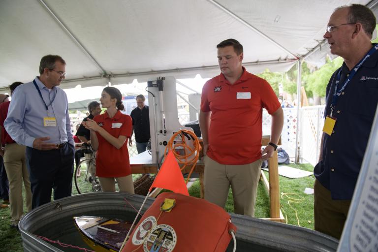 Future Dean David Hahn, interim Dean Larry Head and two students stand around a large metal basin of water with a flotation device and an orange flag in it.