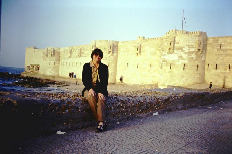 A woman sitting on a short wall with historical buildings in the background