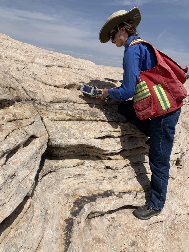 Isabel Barton leans over a rocky hillside holding a small X-ray device.