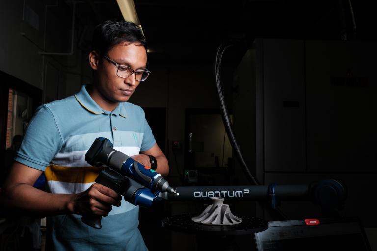 a student holding a drill up to a small 3D printed metal item.