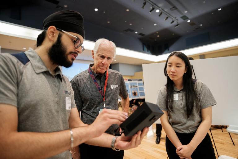 two students show a Design Day judge a small screen.