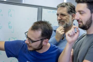 three people look at a whiteboard