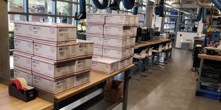 About 40 white boxes, stacked four high, on a table in a laboratory.