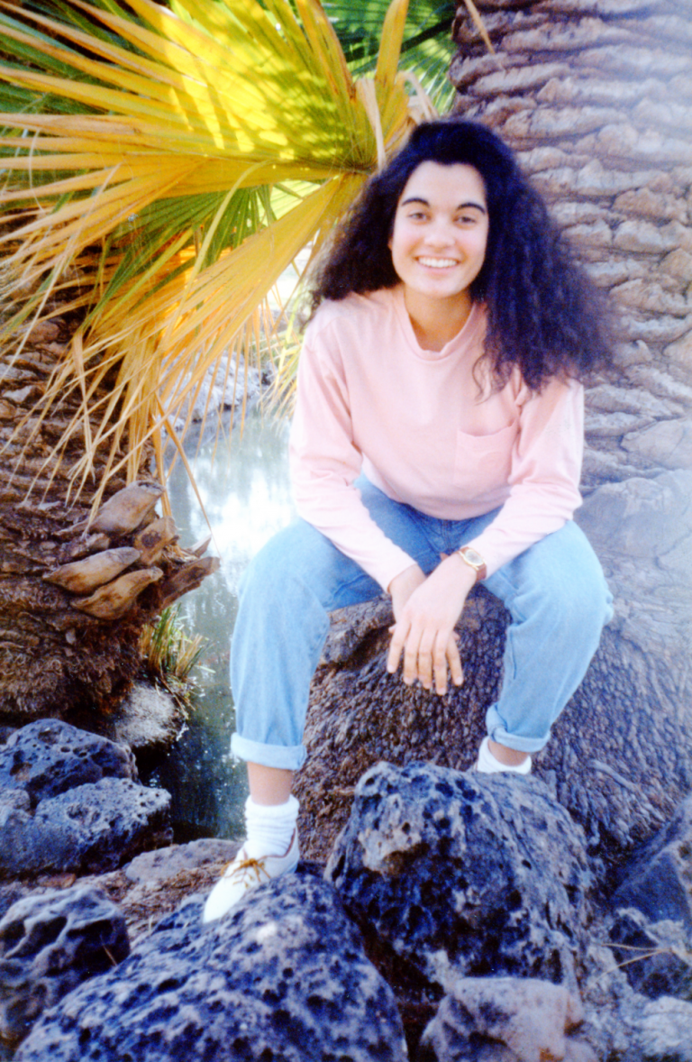 A smiling woman sits in front of a tree.