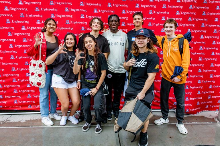 a group of students stands in front of a UA Engineering backdrop and smiles