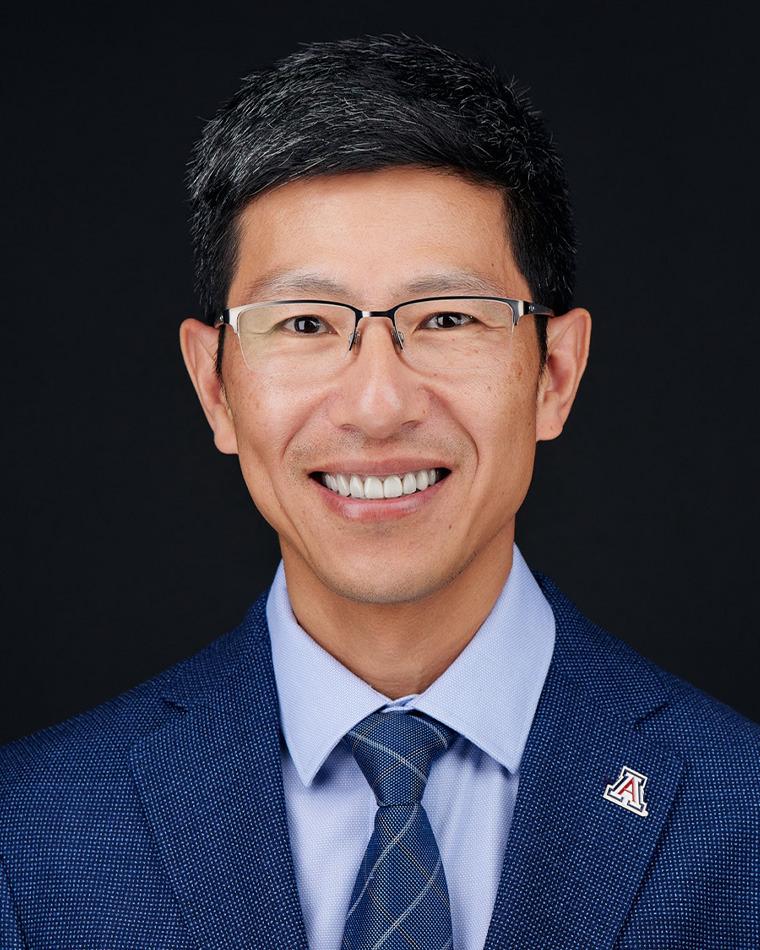 A man with glasses poses for a photo is a light blue shirt and dark blue suit blazer.