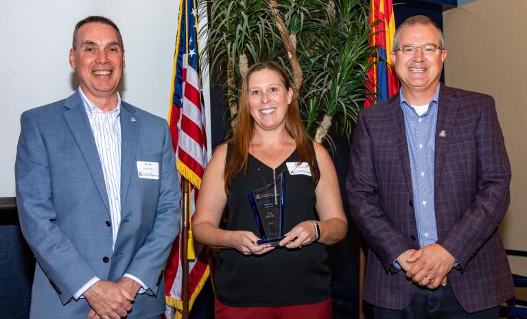 an employee poses with her award, flanked by two presenters