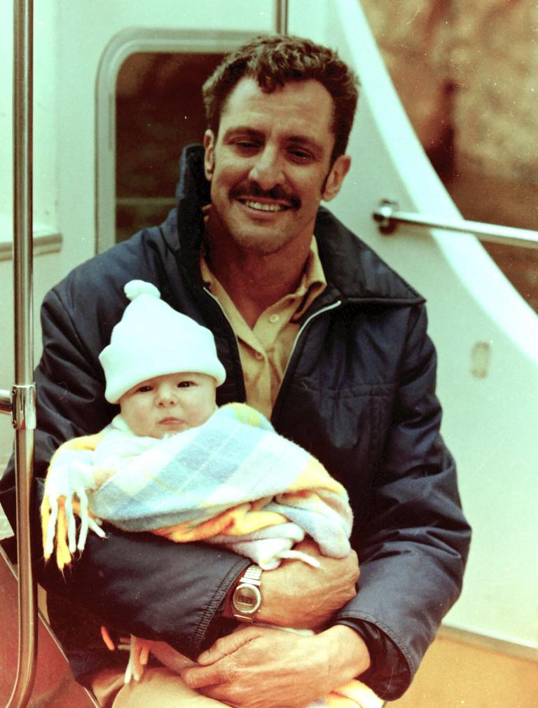 A smiling man holding a baby wearing a small hat.