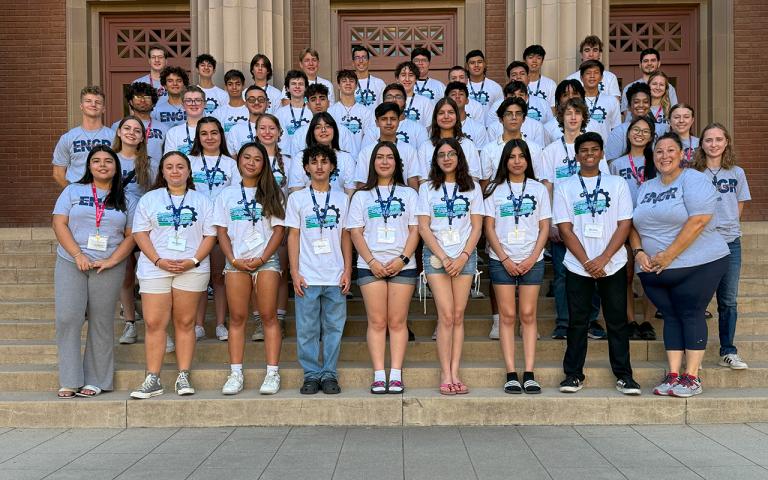 A group of students and an advisor pose for a photo in front of a building.