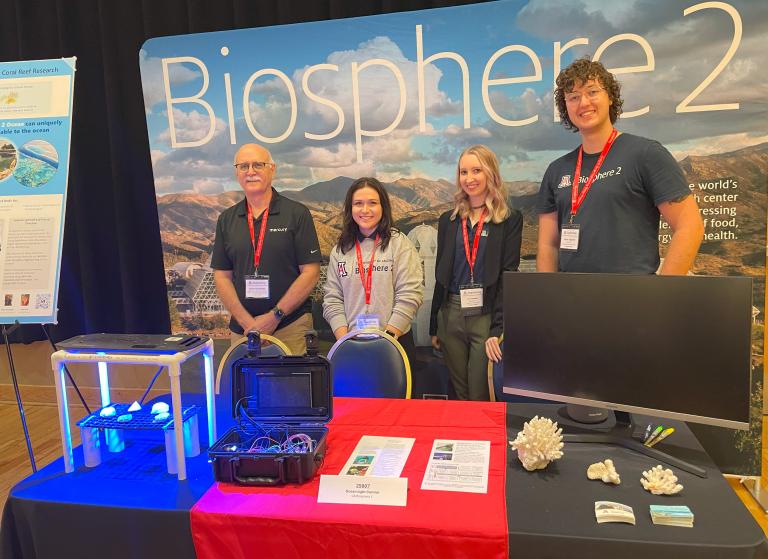 4 people pose in front of a conference display