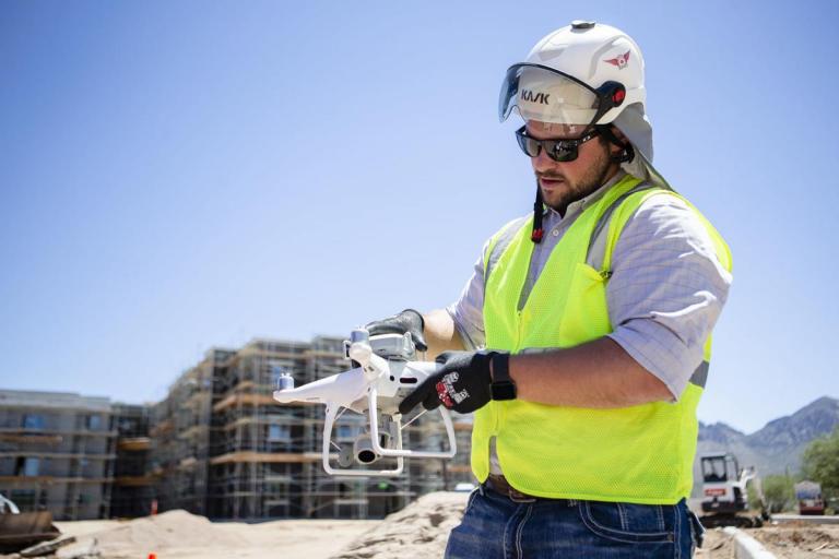 A man in a yellow construction vest and hardhat holds a drone.