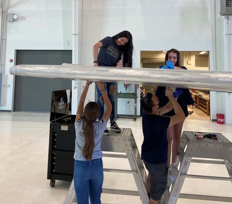 a group of students works on an airplane wing
