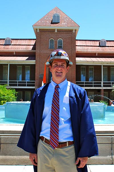 Jeff Tysoe in hardhat and gown in front of the Old Main fountain