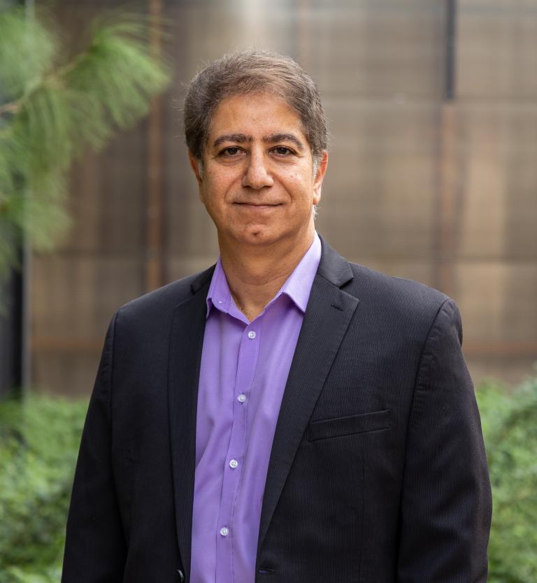 A man poses for a photo with a purple shirt and dark suit blazer.