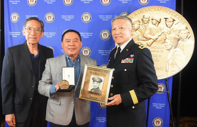 Three people pose with a medal and photo.