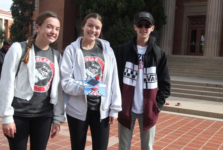 Three students stand outside a university building with their solar tracker
