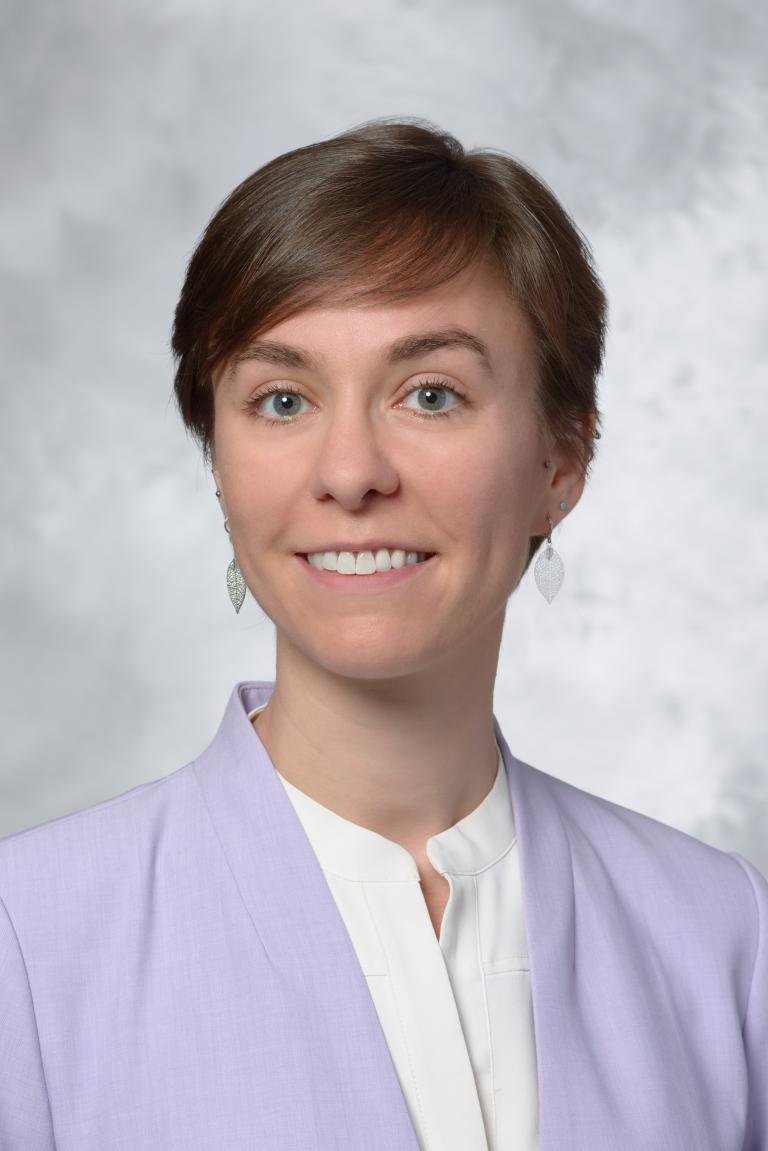 A woman with short dark hair and a purple blazer poses for a photo.