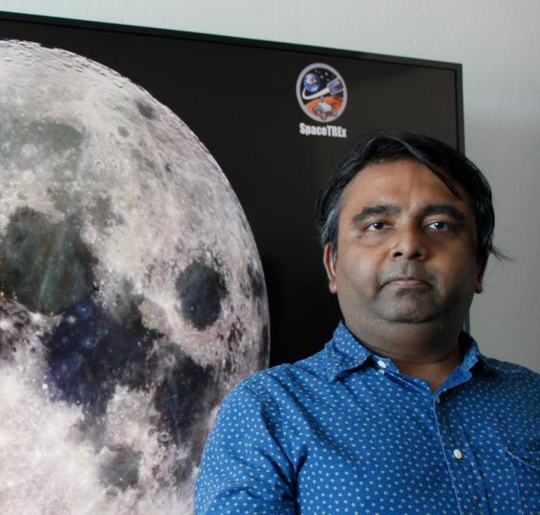 Jekan Thanga, standing in front of a TV screen with a giant image of the moon on it.