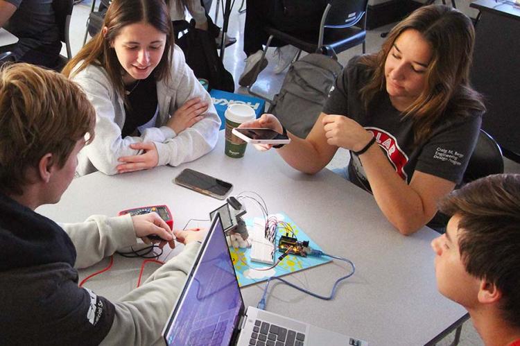 Four students test a small solar device in a classroom