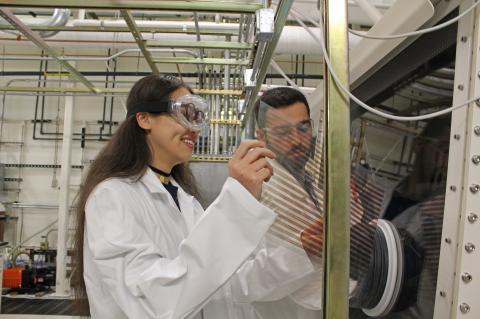 Two students wearing lab coats and goggles in a lab.