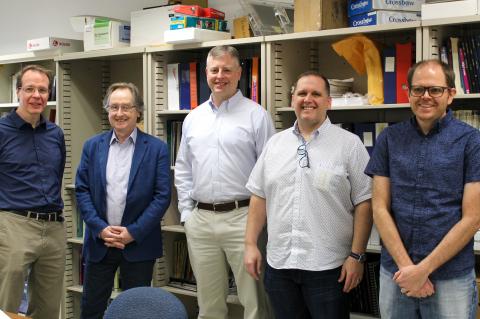 Five men pose for a photo in front of a bookshelf