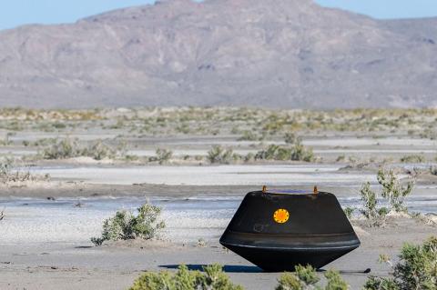 A black metal capsule the size of a doghouse rests on the desert ground