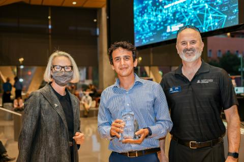 A woman and two men smile for a photo. Sahand Sabet, center, holds a glass award.