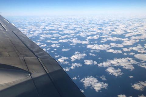 photo taken from a plane showing cumulus clouds from above. The wing of the plane is visible in the left of the frame