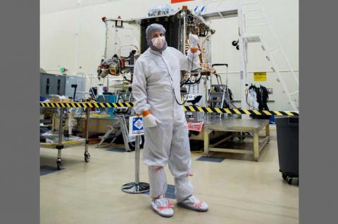 Bradley Williams in a white safety suit in front of a spacecraft.