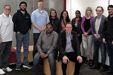 Team members pose in a room with a glass wall and whiteboard