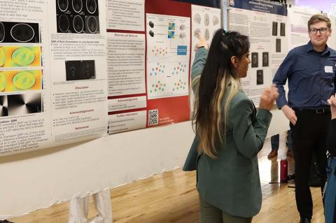 A student gestures at a research poster while two other people look on