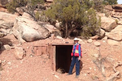 Isabel Barton wearing a red vest and standing next to the entrance of a mine in a desert setting.