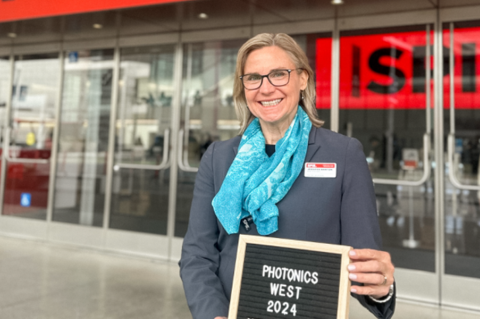 A woman in a blue scarf, Jennifer Barton, holds a sign that reads Photonics West 2024.