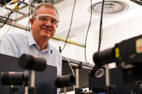 David Hahn smiling and wearing safety glasses, leaned over optics equipment