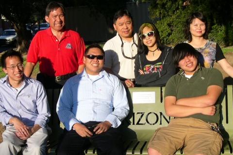 A family group of 7 gathers around a memorial bench on the University of Arizona campus