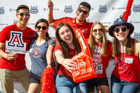 A group of people in Arizona Wildcats gear holding up an inflated #1 finger, pom poms and a UArizona Engineering logo