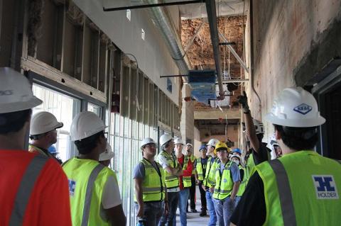 a group of students in hard hats tour an indoor construction site