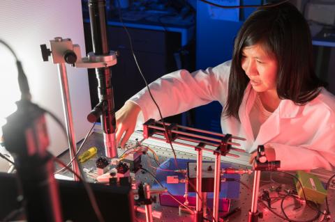 Judith Su wearing a white labcoat and leaned over a complicated array of sensors.