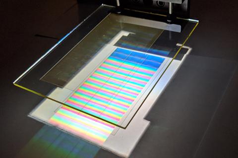 A small piece of glass over a metallic chip, which is reflecting a rainbow of colors.