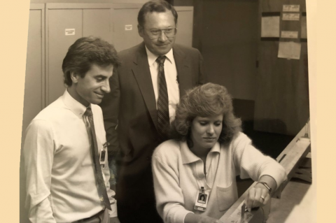 Black and white photo of two men and a woman leaned over a computer