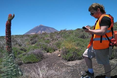 A young man in an orange vests stands in an area with volcanic rock.