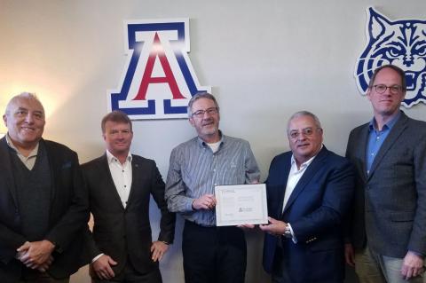 Five men stand in front of a wall with a University of Arizona block A and wildcat logo on it. 